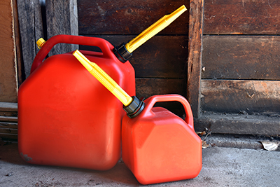 Two red gas cans sit on a sidewalk.