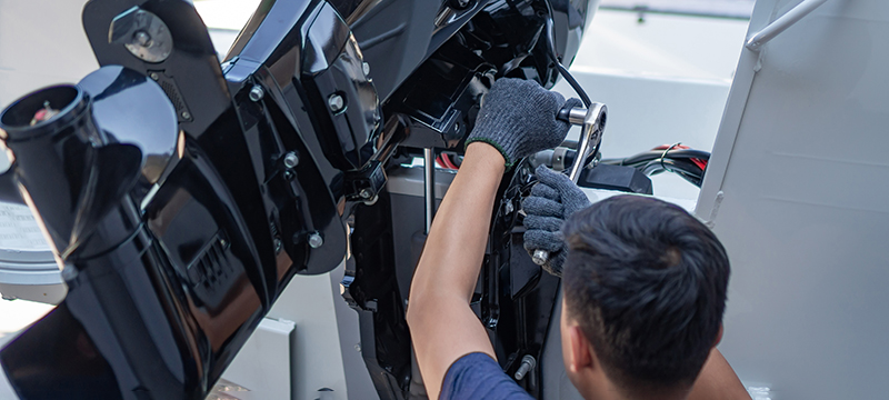 A man uses a ratchet to work on a boat motor.